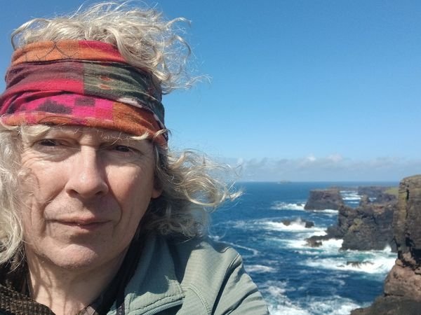 An image of a man standing with the sea behind hi,